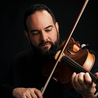 Portrait von Musikschuldirektor Bahram Pietsch vor dunklem Hintergrund mit seinem Instrument