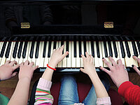 Hände von 2 Kindern und einer erwachsenen Person auf einer Klavier-Tastatur