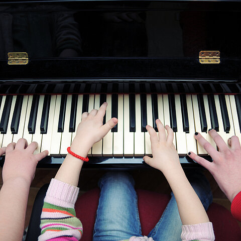 Hände von 2 Kindern und einer erwachsenen Person auf einer Klavier-Tastatur