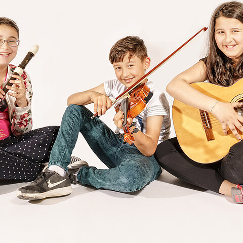 Kinder im Schneidersitz mit Blockflöte, Violine und Gitarre.