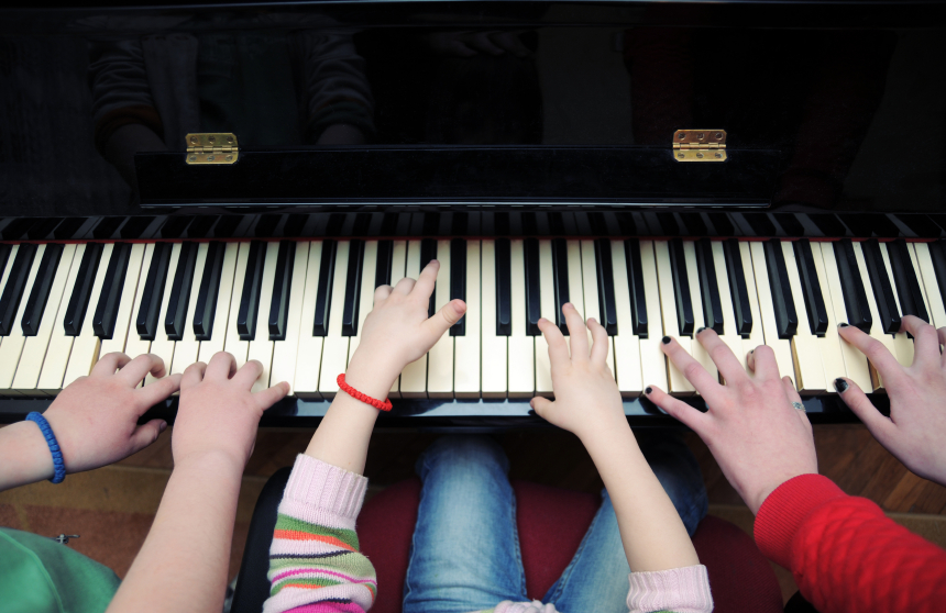 Hände von 2 Kindern und einer erwachsenen Person auf einer Klavier-Tastatur